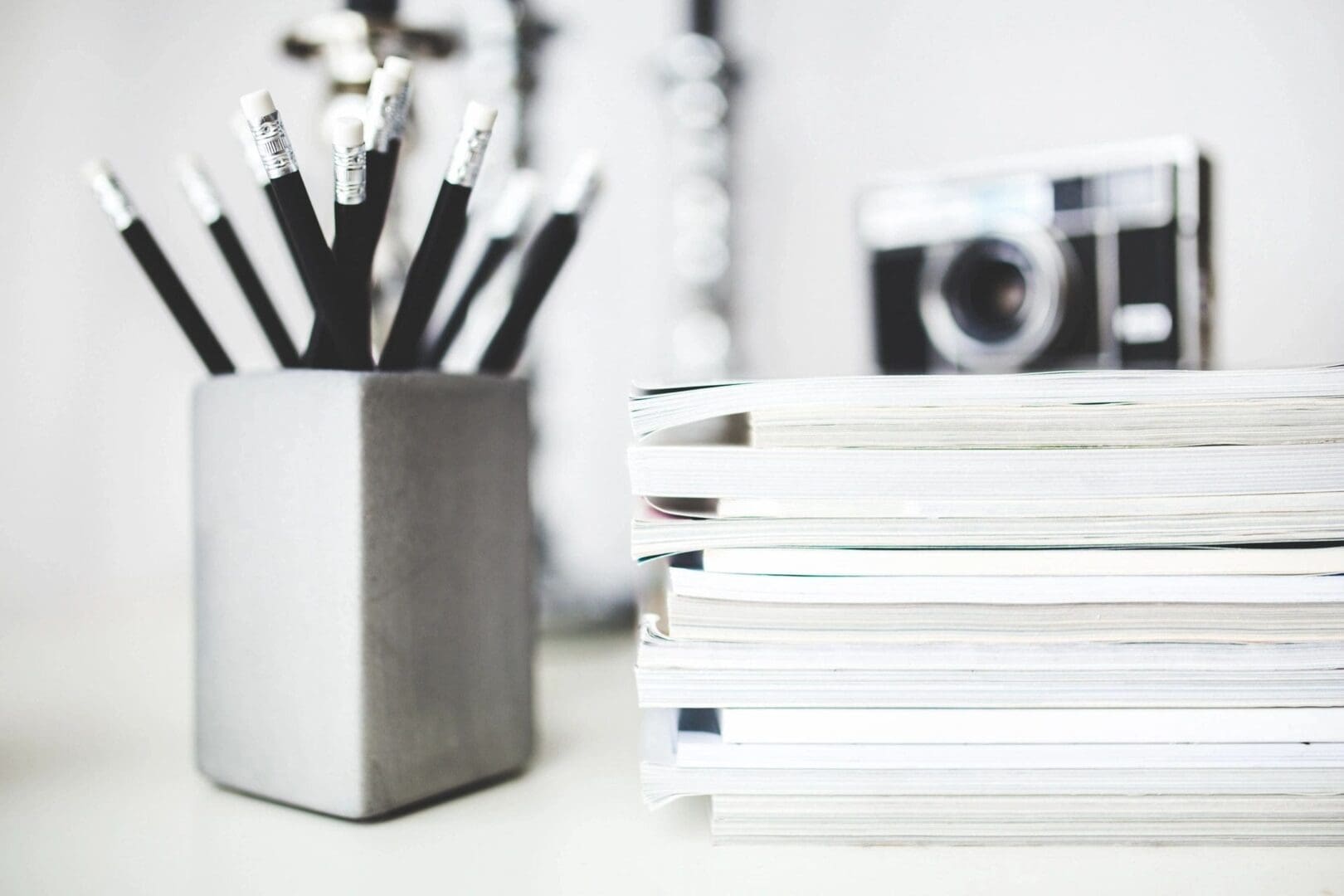Stack of white notebooks and a container with pencils on a desk.