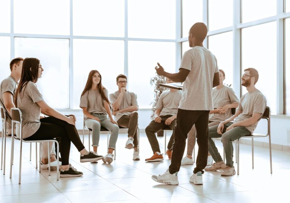 A person leading a discussion with a group seated in a bright room.