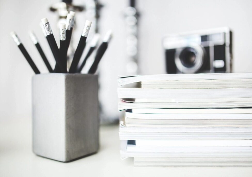 Stack of white notebooks and a container with pencils on a desk.